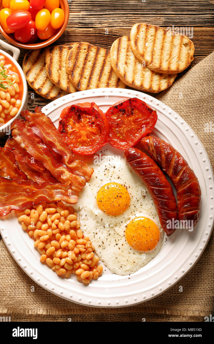English Breakfast with sausages, grilled tomatoes, egg, bacon, beans and bread on white plate Stock Photo