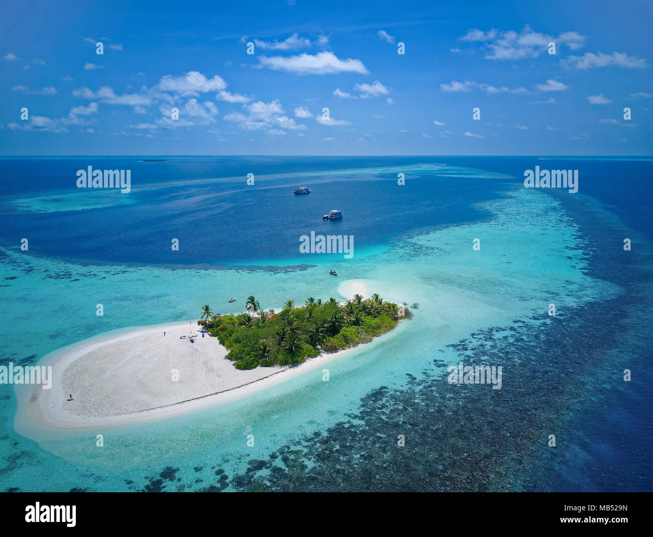 Uninhabited palm island, sandy beach all around, offshore coral reef, diving boat in the back, Ari atoll, Indian Ocean, Maldives Stock Photo