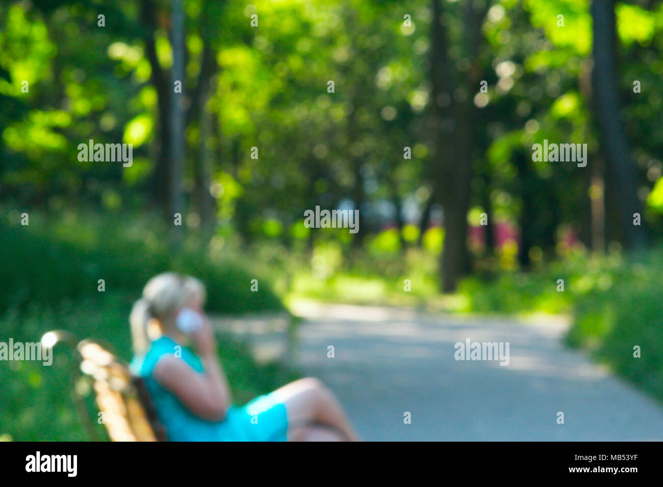Young girl sitting on bench in city park and talking on phone ...