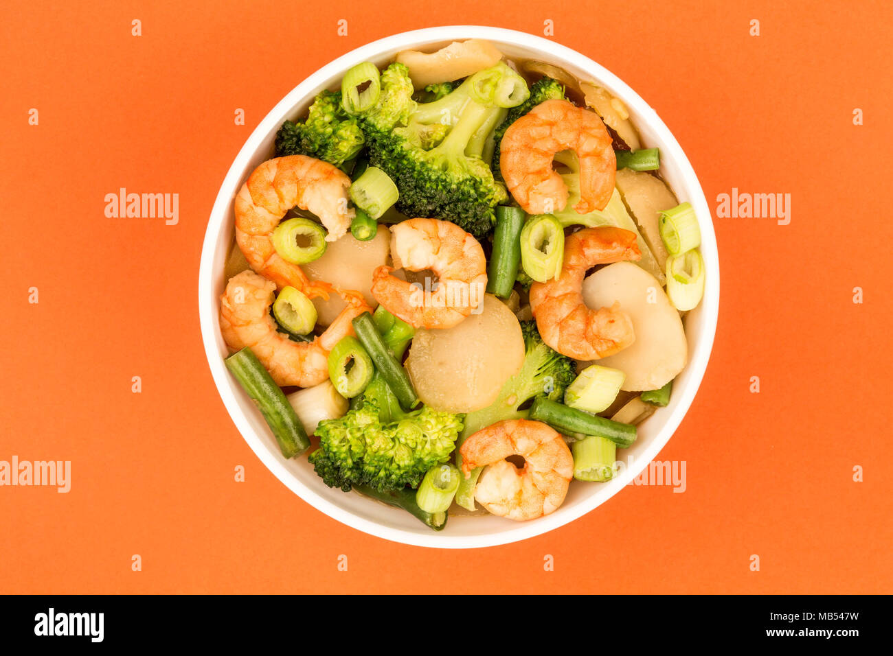 Chinese Style King Prawn With Ginger Broccoli And Spring Onions Against A Red Background Stock