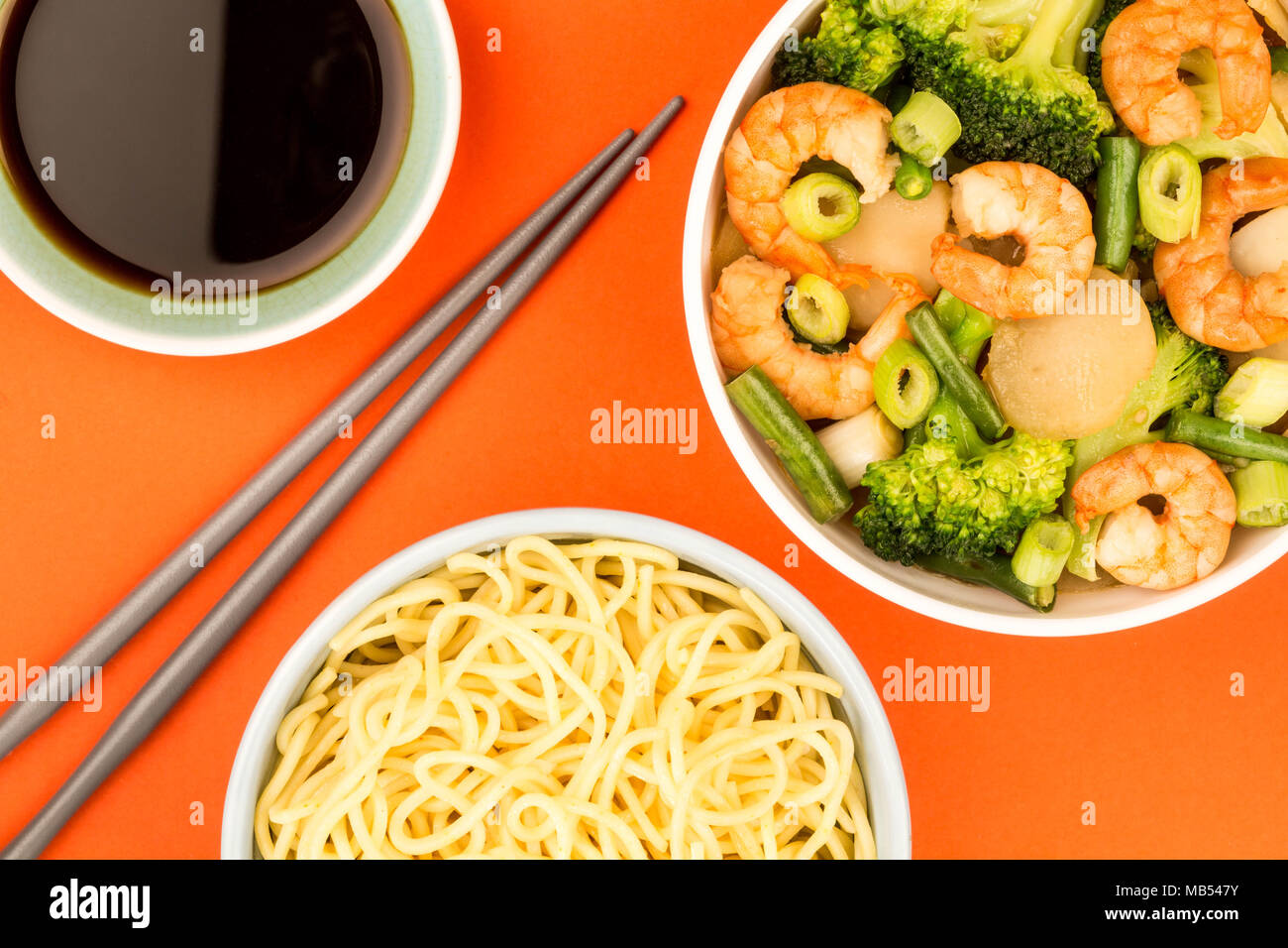 Chinese Style King Prawn With Ginger Broccoli And Spring Onions Against A Red Background Stock