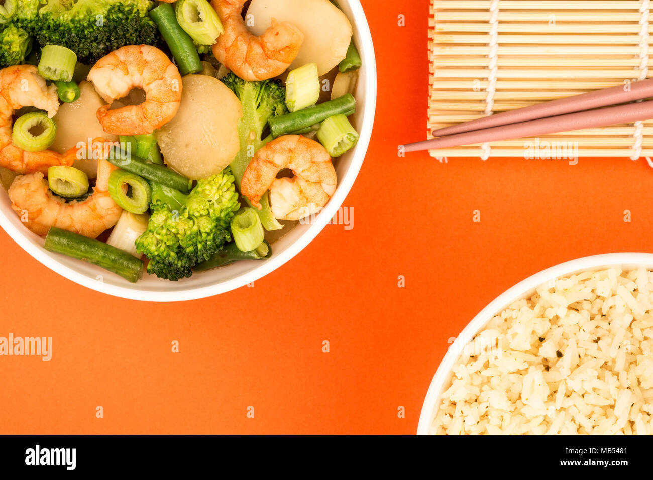 Chinese Style King Prawn With Ginger Broccoli And Spring Onions Against A Red Background Stock