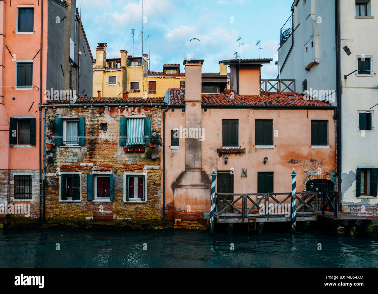 Facade of partially mossy old brick house with wooden vintage door on narrow canal in Venice, Italy Stock Photo