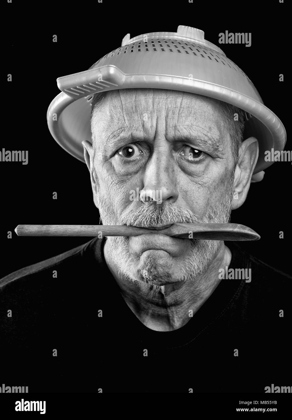 Dramatic black and white Portrait of a mad man with a plastic strainer on the head and a wooden spoon in the mouth Stock Photo