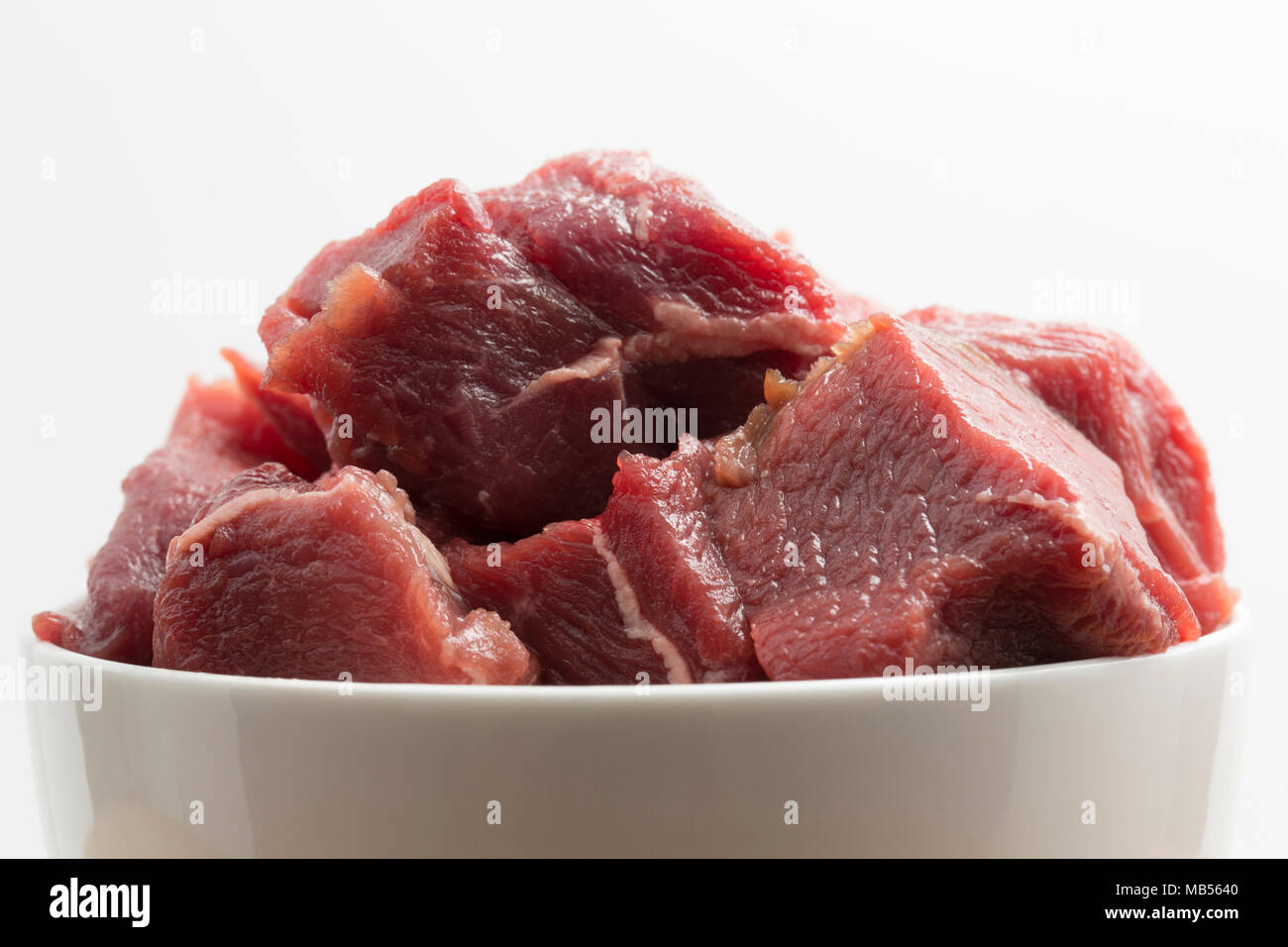 Diced raw shoulder meat from a wild boar, Sus Scrofa, from a boar shot in Tuscany, Italy, before cooking.  On a white background. The meat is much dar Stock Photo