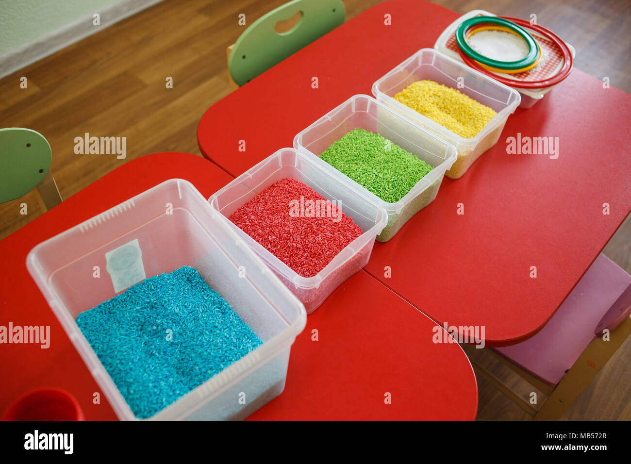 Sensory bin for toddlers with colourful rice on red table. Universal