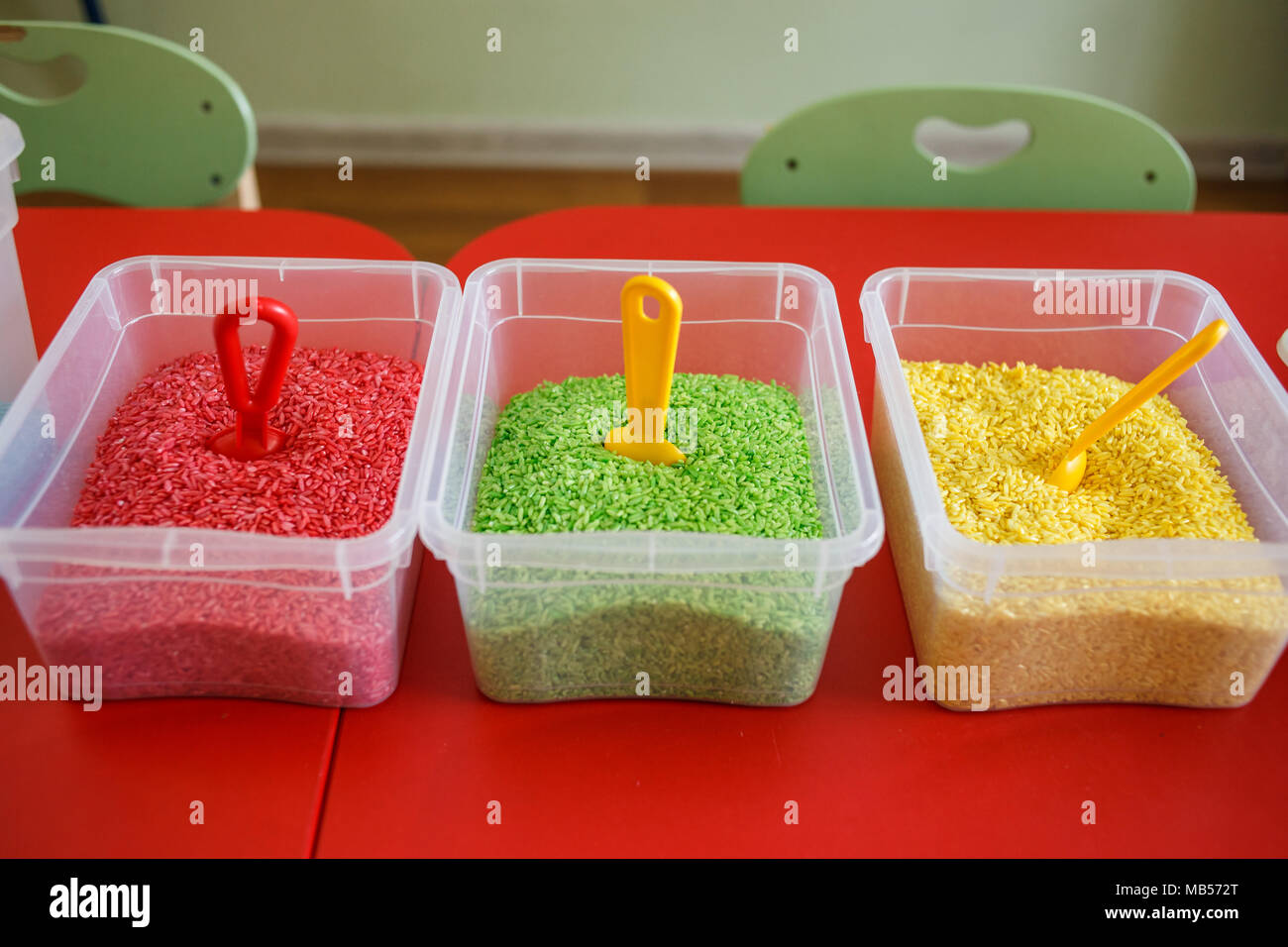 Sensory bin for toddlers with colourful rice on red table. Universal educational game in