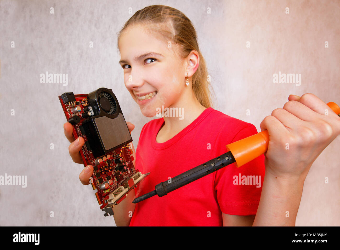 Joke, parody: angry teenage girl fiercely pokes a soldering iron into a computer video card. Generalized-misunderstanding of the device malfunction, t Stock Photo