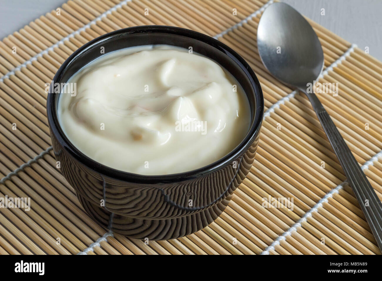 Creamy fruit yogurt in black bowl on reed table mat close up Stock Photo