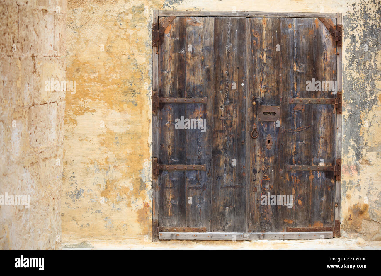 Closed old wooden door with metal rusty mail box opening and details on a weathered yellow wall, space for text. Mdina, Malta Stock Photo