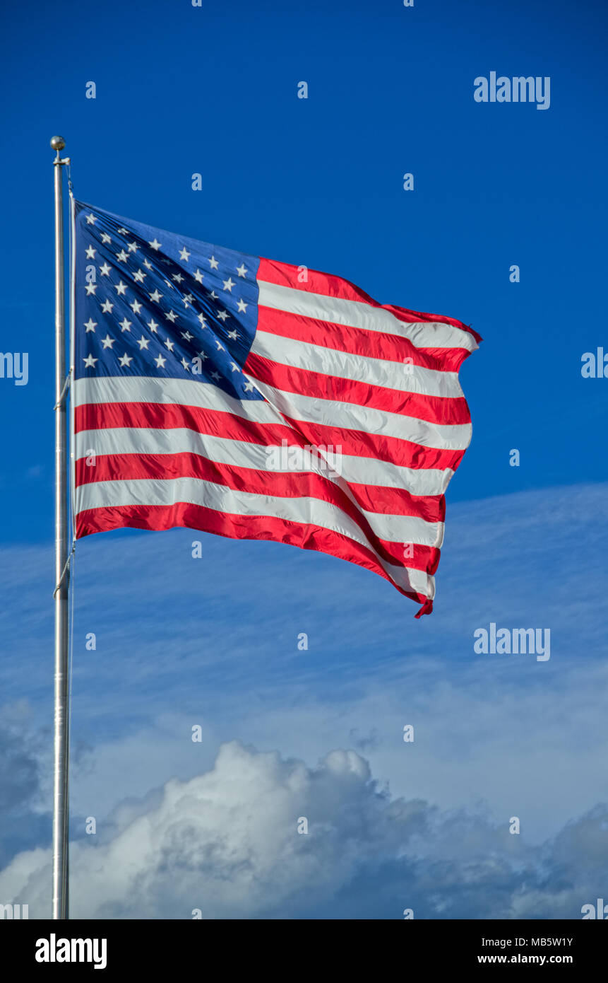 A very large American flag flies above the clouds on a beauty sunny
