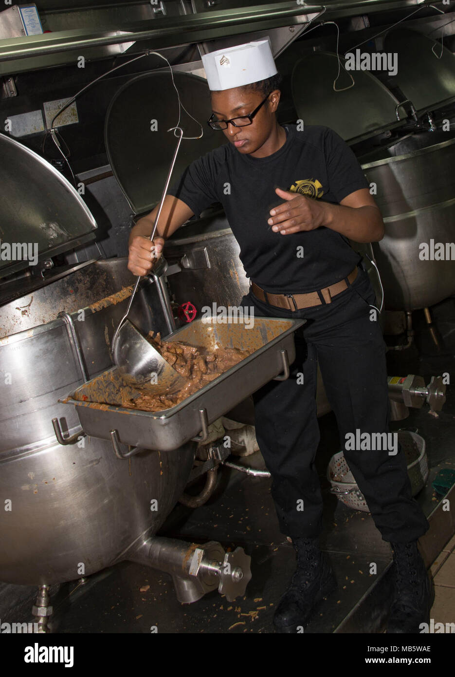OCEAN (Feb. 22, 2018) Marine Sgt. Tandra Burns, from Flint, Michigan, ladles pepper steak into a serving pan in the galley of the Wasp-class amphibious assault ship USS Iwo Jima (LHD 7), Feb. 22, 2018. Iwo Jima, homeported in Mayport, Florida, is conducting naval operations in the U.S. 6th Fleet area of operations. Stock Photo