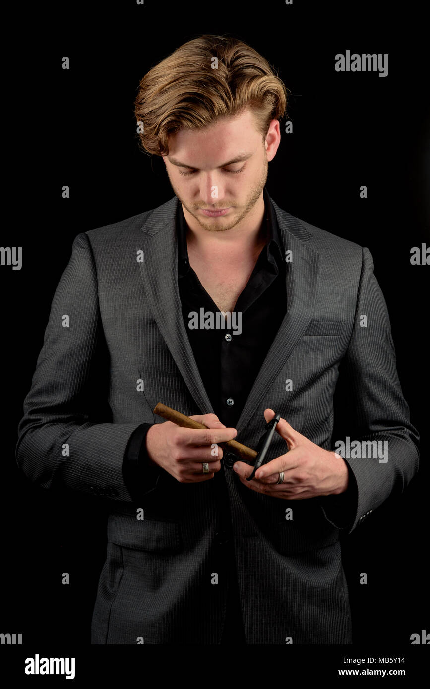 Caucasian male model in a charcoal suit cutting a fresh cigar.  Model isoalted againt a black background Stock Photo