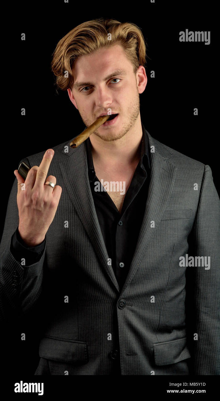 Caucasian male model in a charcoal suit with a fresh cigar. Model Flipping off the camera. Model isoalted againt a black background Stock Photo