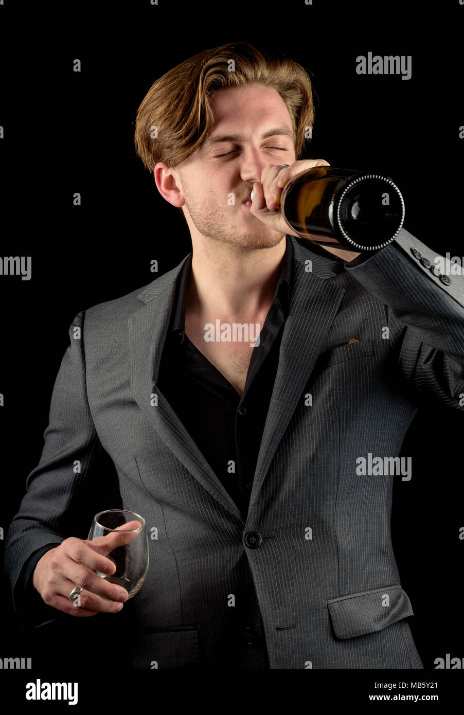 Caucasian male model in a charcoal suit with a bottle of red wine and a fresh cigar. Model isoalted againt a black background Stock Photo