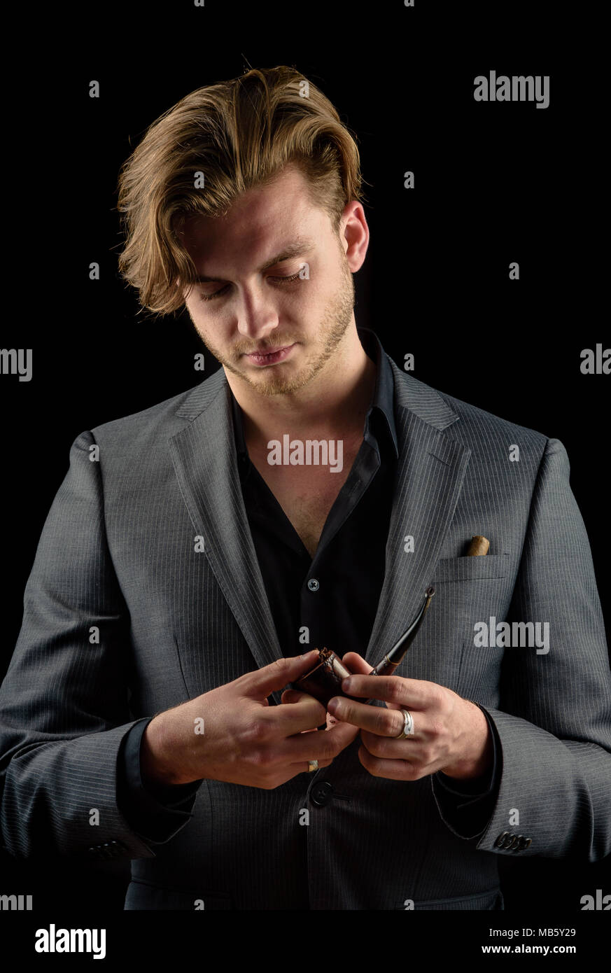 Caucasian male model in a charcoal suit packing a pipe with tobacco Stock Photo