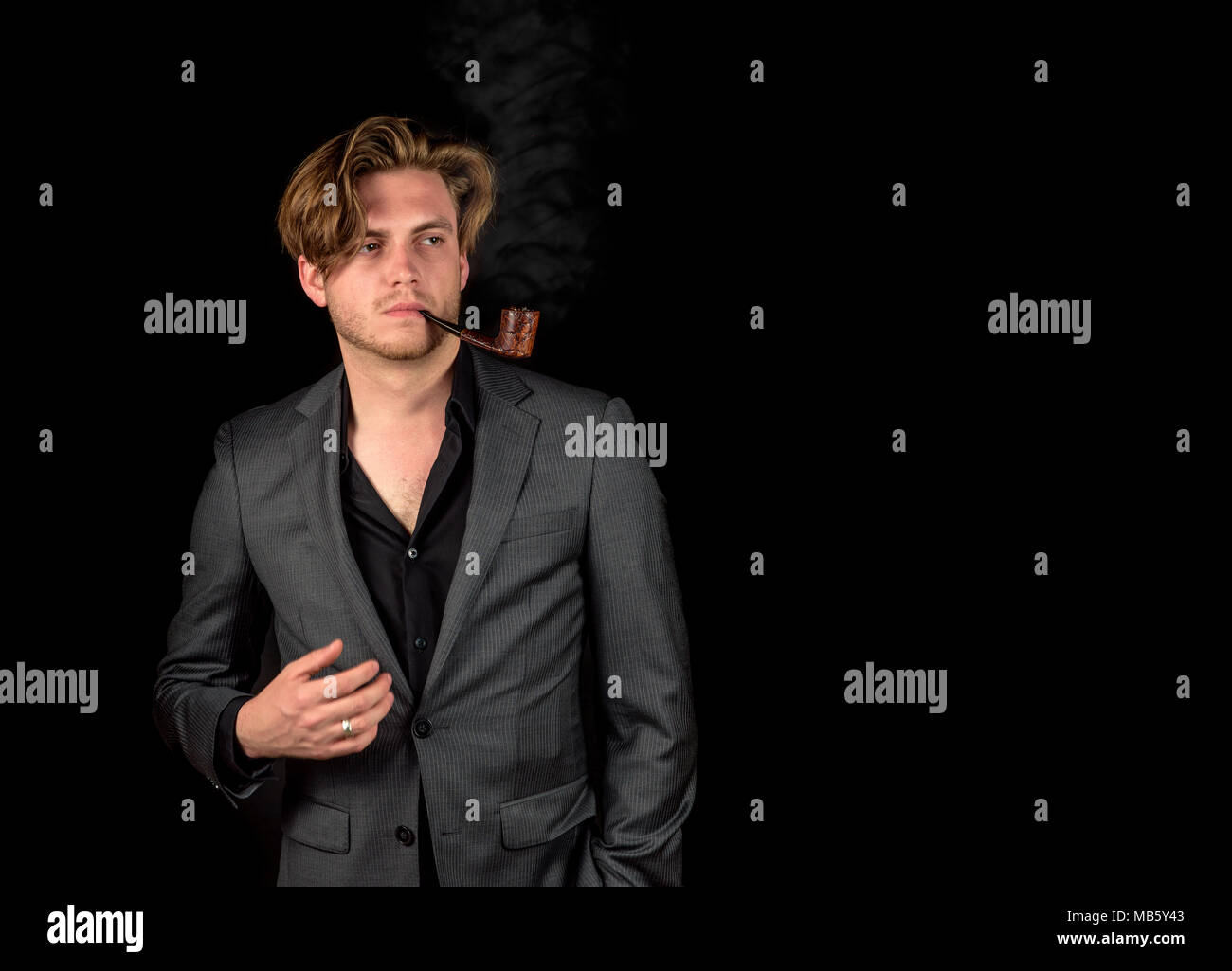 Caucasian male model in a charcoal suit. Model smoking a wooden pipe Stock Photo