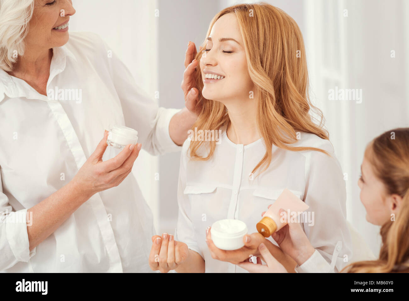 Careful grandma and daughter applying cream on moms face Stock Photo
