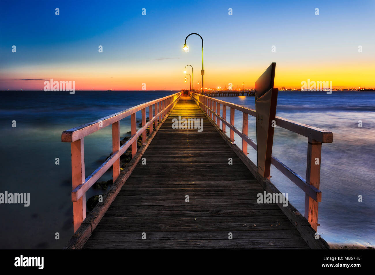 Lagoon pier made of timber in Port Melbourne at sunset. Empty abandoned sandy beach on Port Phillip bay of Melbourne city facing orange sky of setting Stock Photo