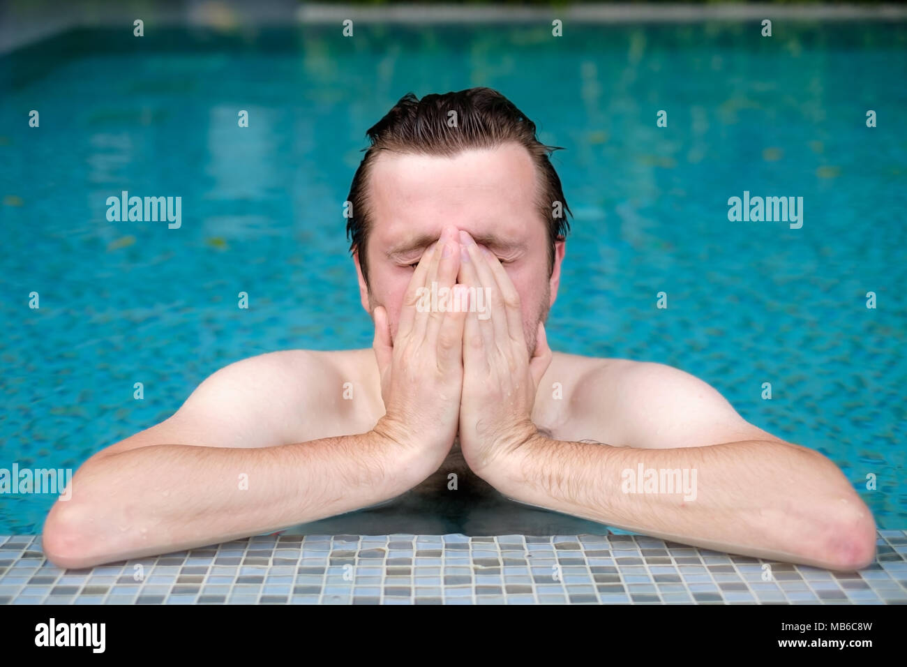 A young man in the pool wipes his face with his hand. He is allergic to