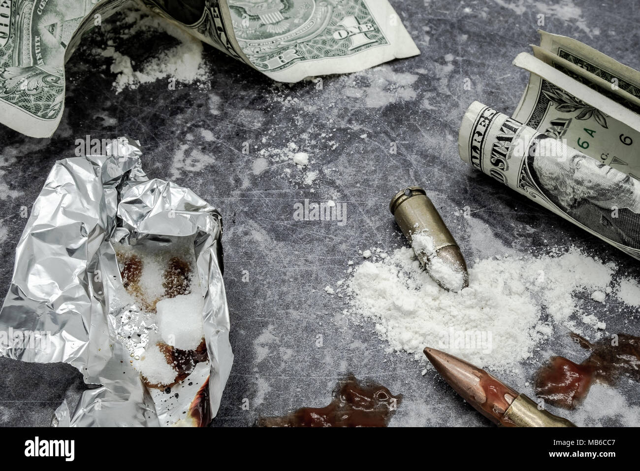 Mock-up concept if illegal drug dealing on a work surface. Showing dollar bills, mock-up bullets together with prop blood together with smoking foil. Stock Photo