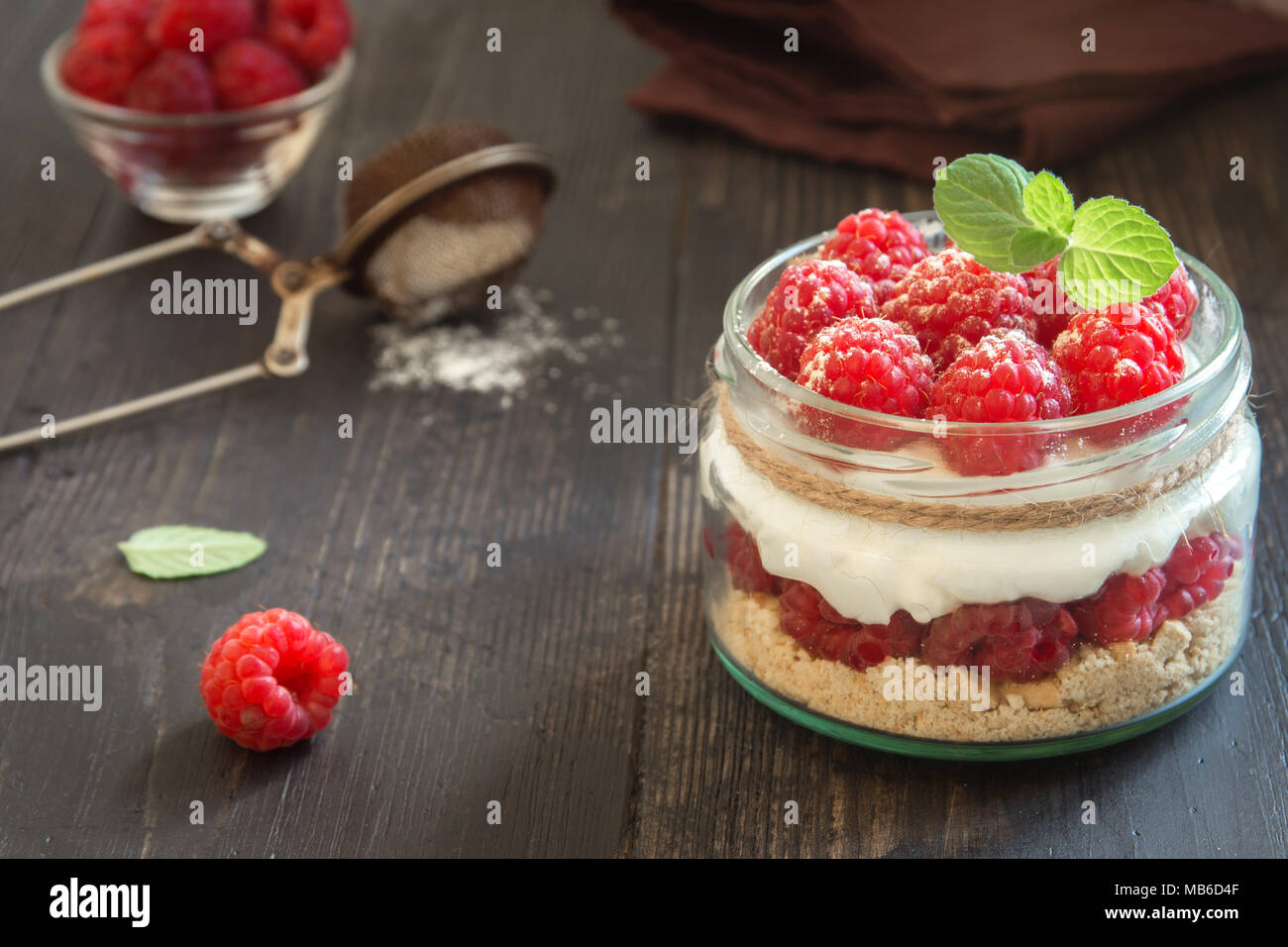 Raspberry cheesecake dessert in glass jar with fresh raspberries and cream cheese on wooden background. Healthy homemade summer berry layered dessert. Stock Photo