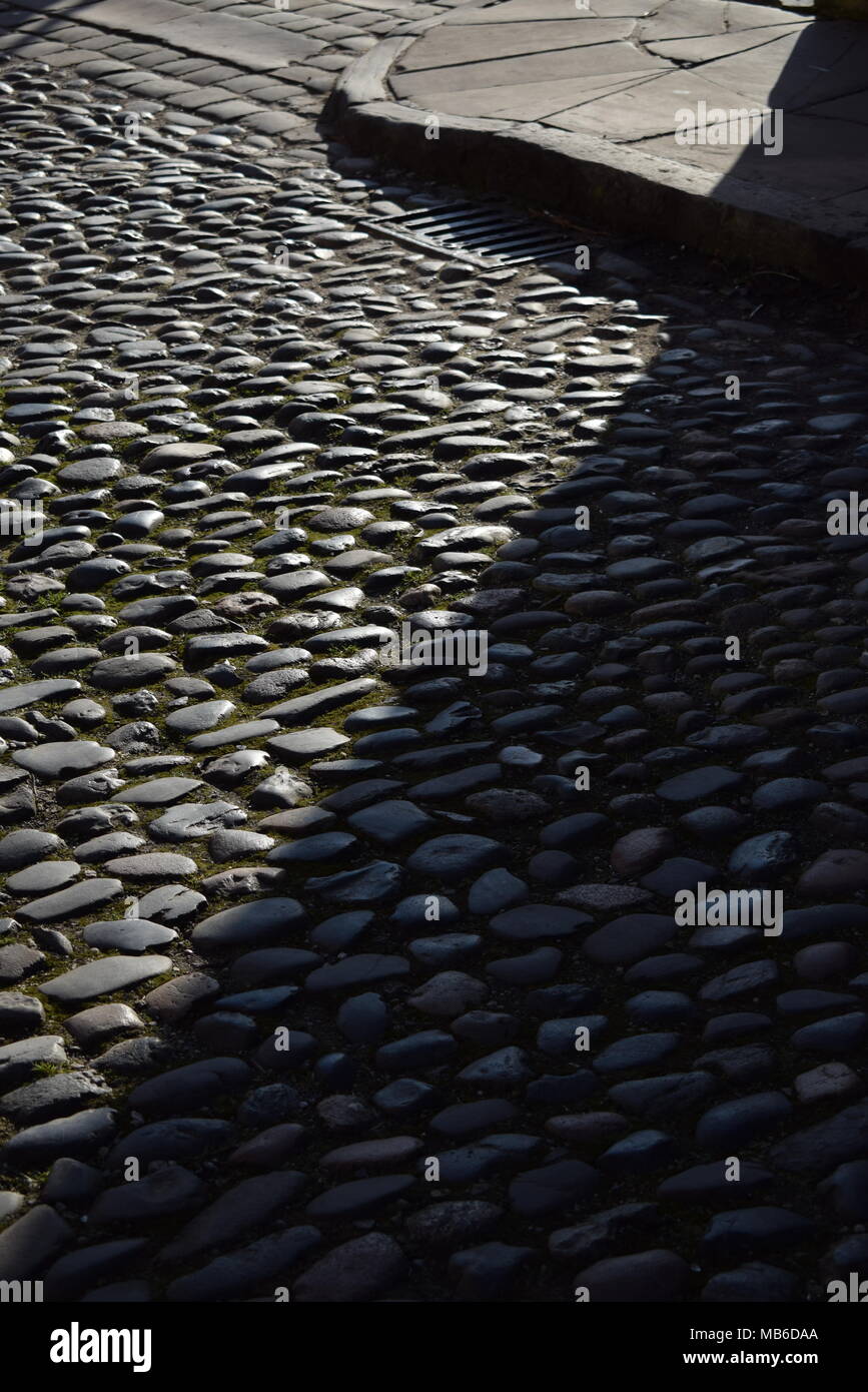 A section of Chester's cobbled Abbey street from behind the Cathedral with the early morning sunshine cutting away at a shadow Stock Photo