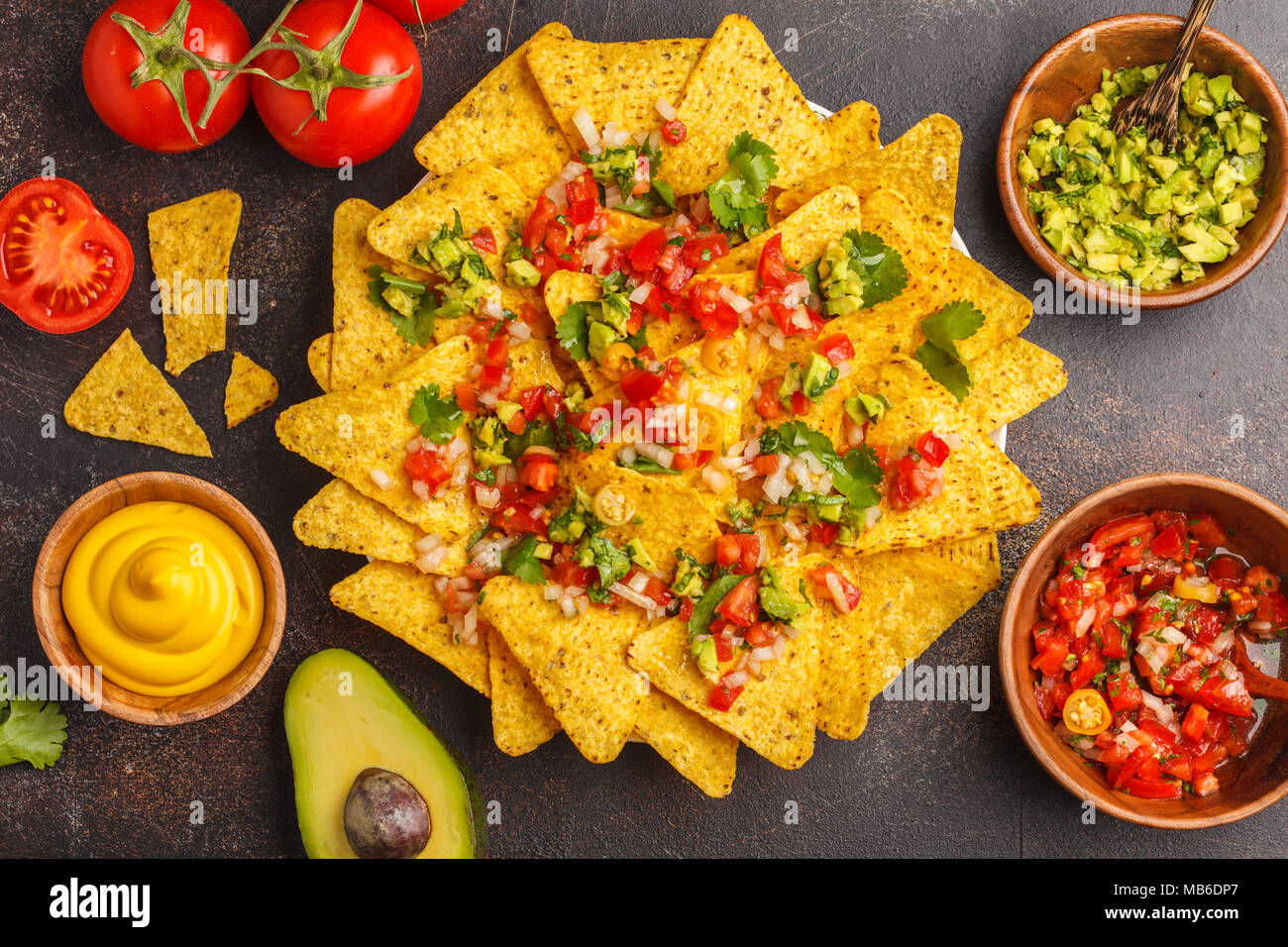 Mexican food concept. Nachos - yellow corn totopos chips with various sauces in wooden bowls: guacamole, cheese sauce, pico del gallo Stock Photo