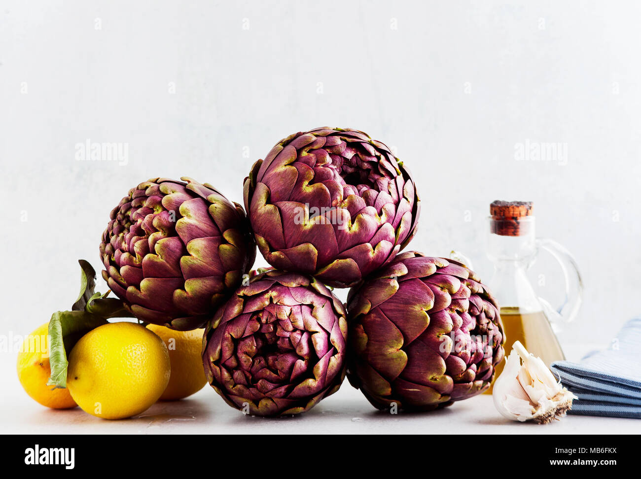 Fresh bunch of purple artichokes on white background with lemon, olive oil , garlic . spring