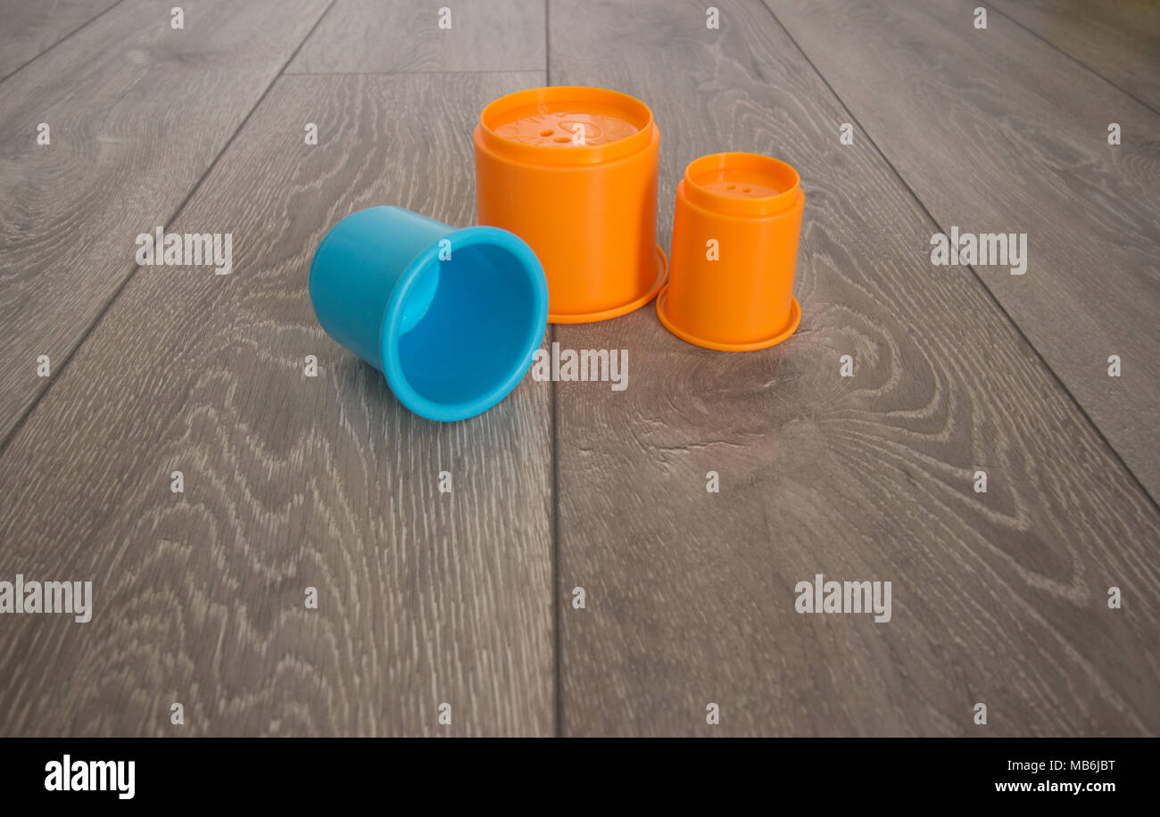 Three plastic stacking cup toys for children on a grey wooden floor with wood grain Stock Photo