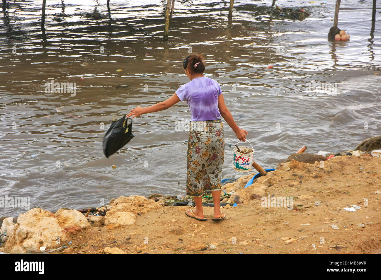 Local woman throwing garbage in the sea in Labuan Bajo town, Flores Island, Nusa Tenggara, Indonesia. The local economy in the town is centered around Stock Photo