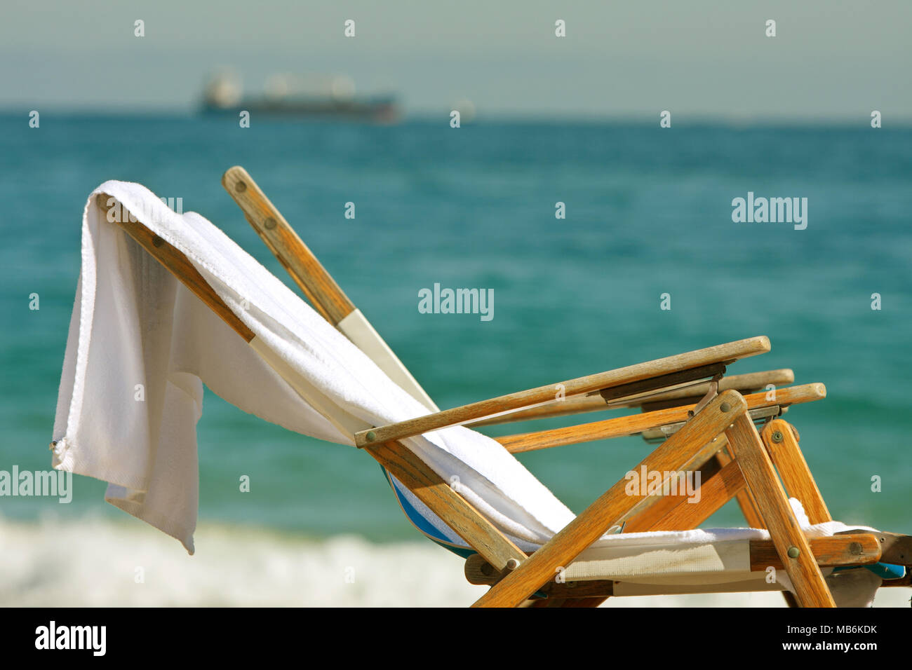 Two wooden deck chairs with towels slung over them sit on Florida beach