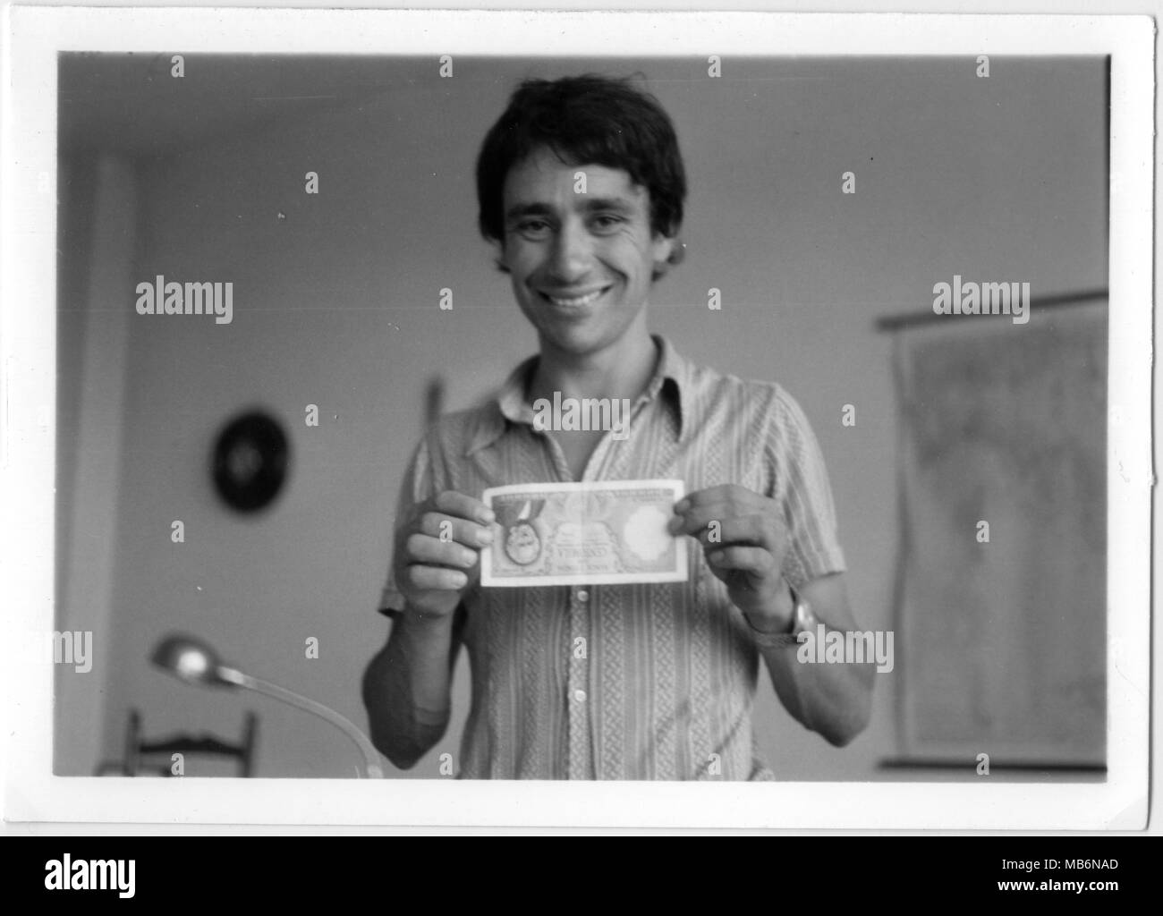 Young man happy smiling keeping an old 100 Lire italian bill with his hands. 1970s black and white. Italy office Stock Photo