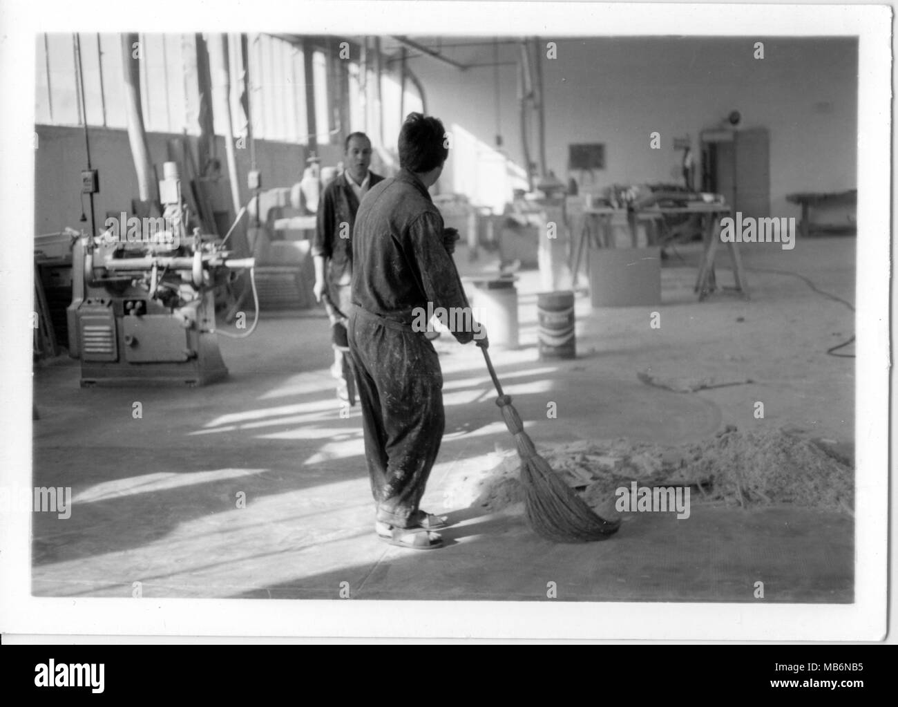 Young man cleaning an old 1970s factory with his boss cheking his work. Old job.  Italy Stock Photo
