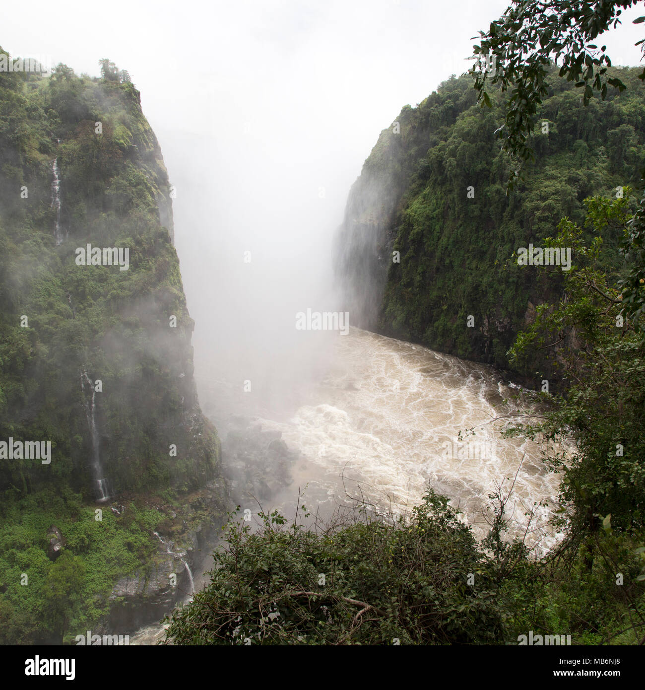 Misty spray caused by the Victoria Falls on the border of Zimbabwe and Zambia. The swirling water of the River Zambezi flows in the gorge. Stock Photo