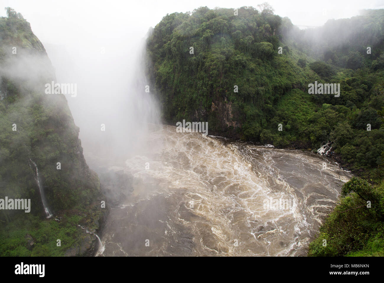 Misty spray caused by the Victoria Falls on the border of Zimbabwe and Zambia. The swirling water of the River Zambezi flows in the gorge. Stock Photo