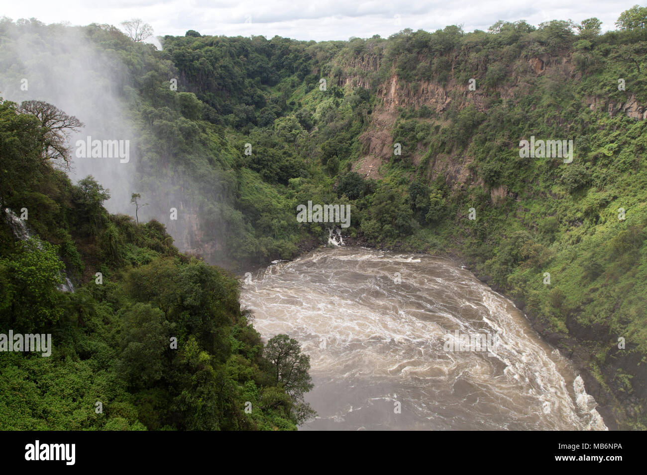 Misty spray caused by the Victoria Falls on the border of Zimbabwe and Zambia. The swirling water of the River Zambezi flows in the gorge. Stock Photo