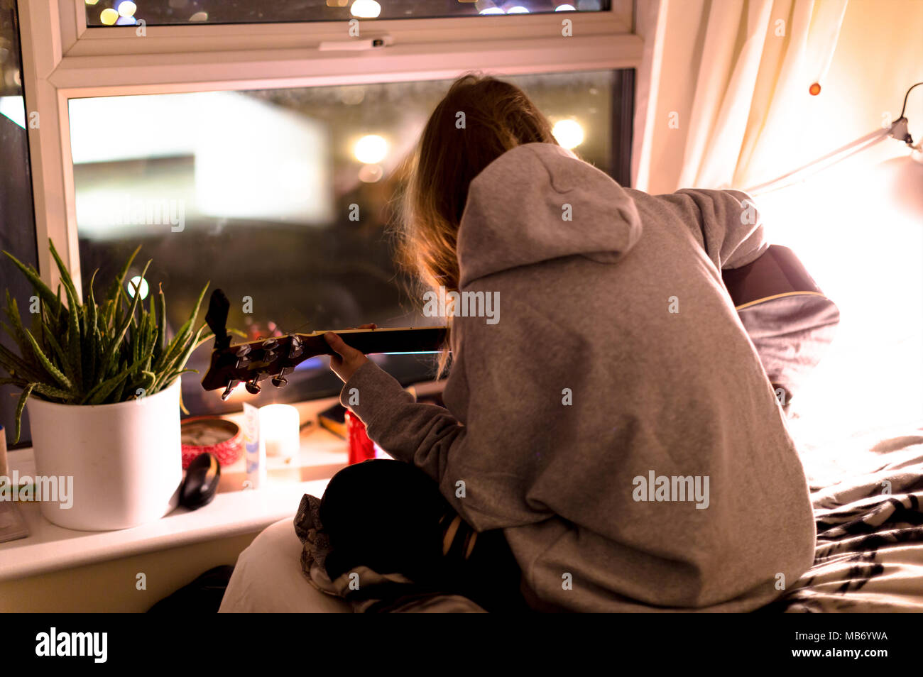 Girl playing a guitar next to the window Stock Photo