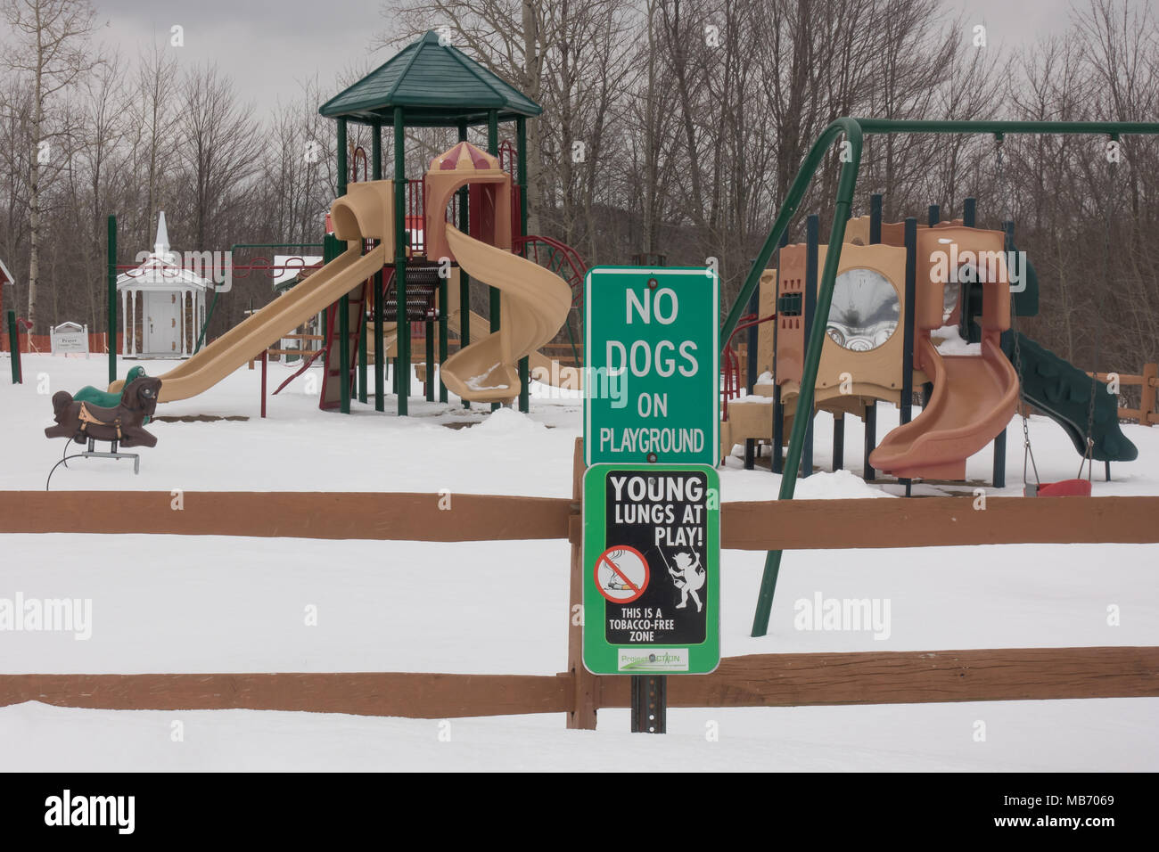 Snow covered playground in Speculator, NY USA with signs indicating no dogs and no smoking on the playground. Stock Photo