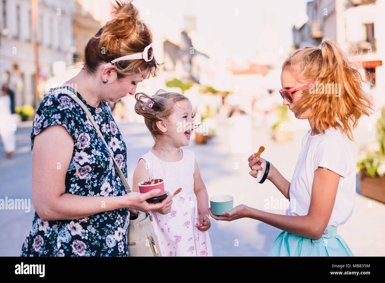 Family spending time together in the city centre enjoy eating ice cream on a summer day. Mother, toddler and teenage girl spending quality time Stock Photo