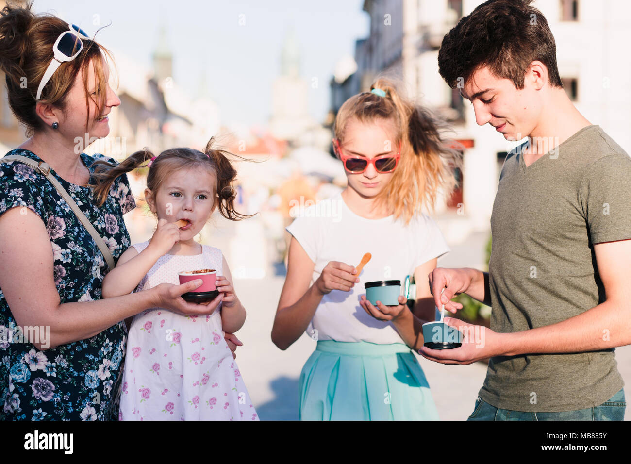 Family spending time together in the city centre enjoy eating ice cream on summer day. Mother, toddler and teenage girl and boy spending quality time Stock Photo