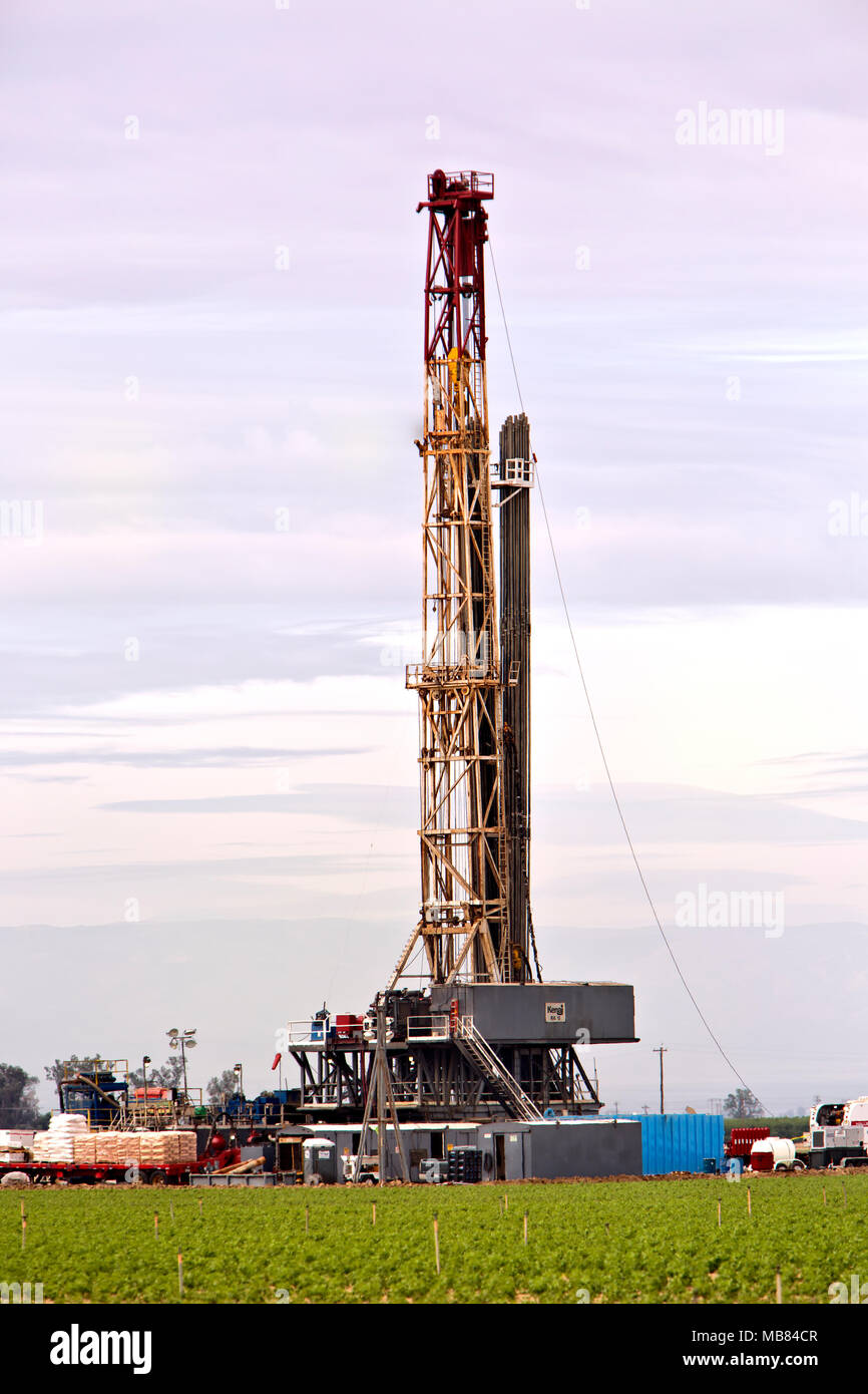 Drilling rig operating in productive tomato field in foreground,  oil exploration. Stock Photo