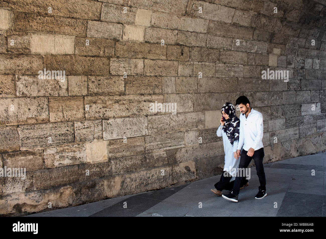 Young muslim couple walk hand in hand in front of old, stone wall in Eminonu /Sirkeci area of Istanbul. Stock Photo