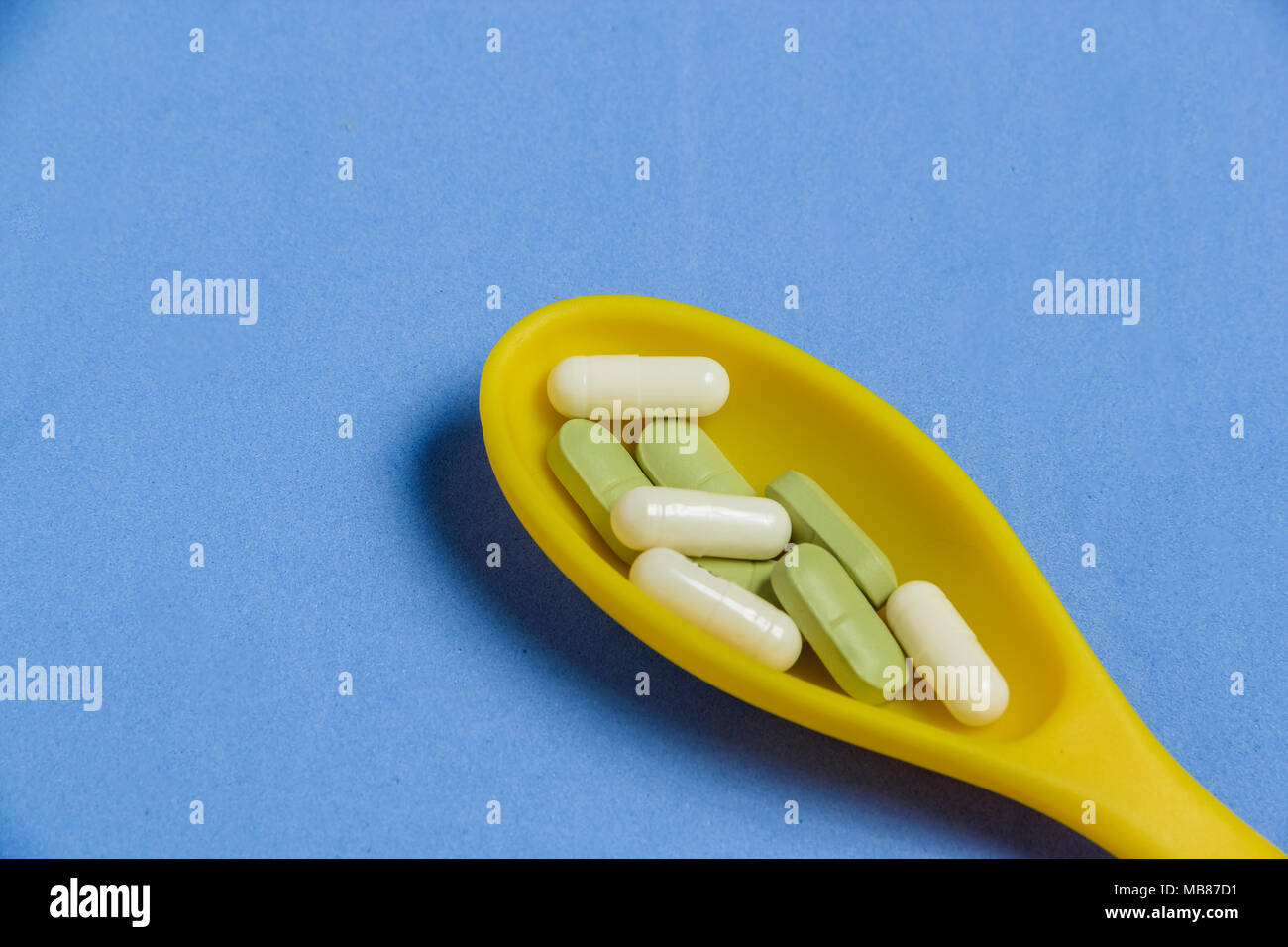 Pills and Capsules in Yellow Spoon on Blue Table. Stock Photo