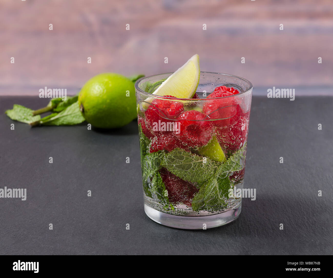 Raspberry lemonade with lime and mint in a glass. Non-alcoholic raspberry refreshment drink. Raspberry mojito in a glass with mint and lime. Stock Photo