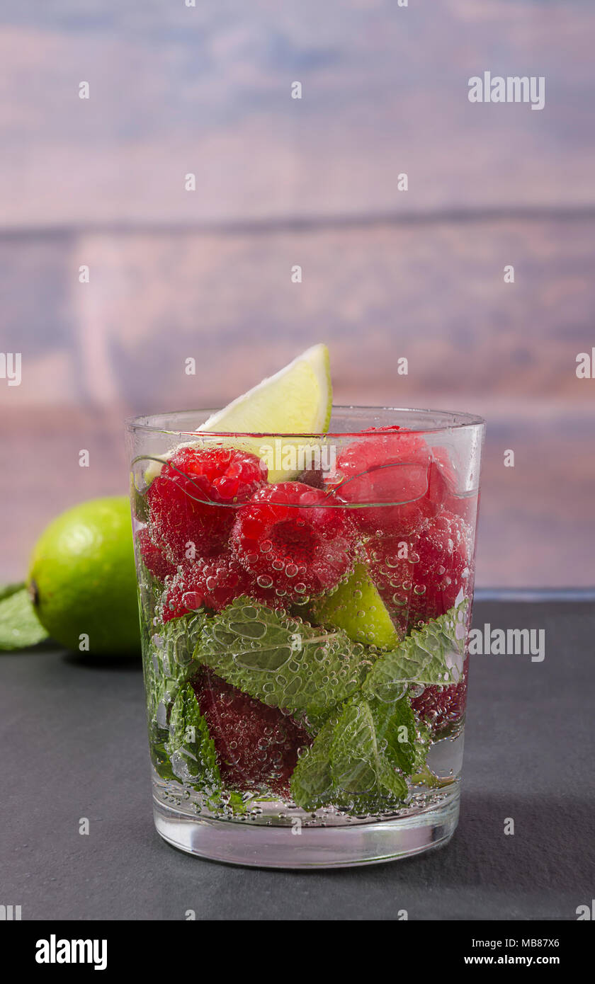 Raspberry lemonade with lime and mint in a glass. Non-alcoholic raspberry refreshment drink. Raspberry mojito in a glass with mint and lime. Stock Photo