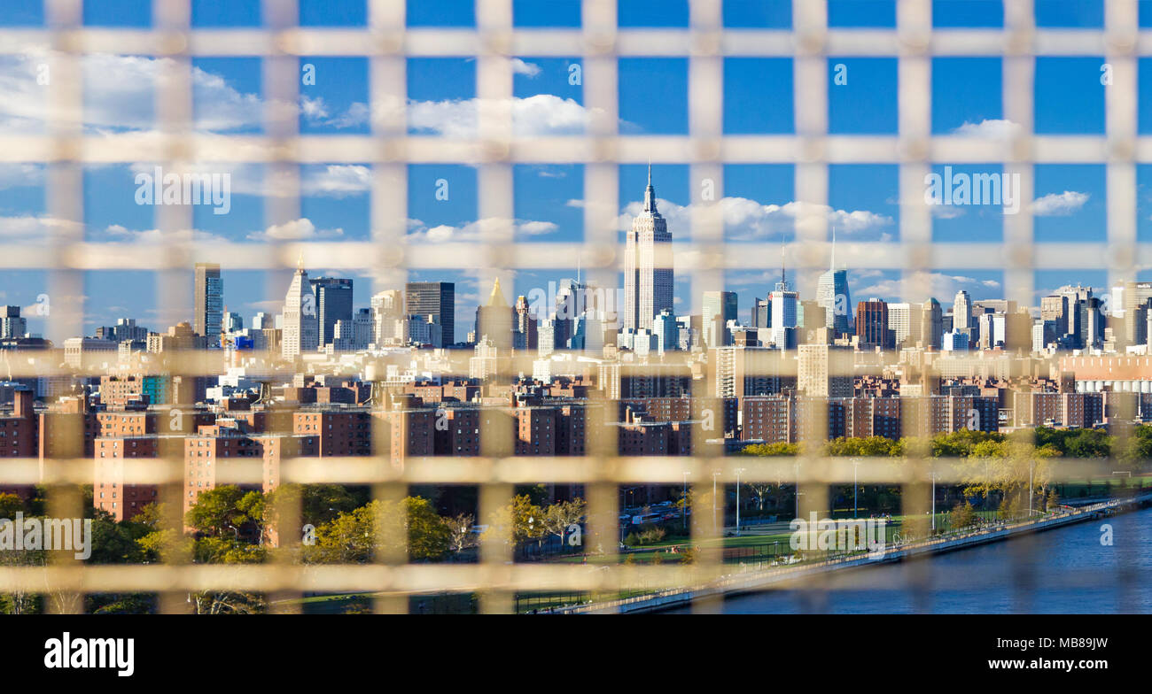 New York City skyline seen through the bars of a fence on the Williamsburg Bridge between