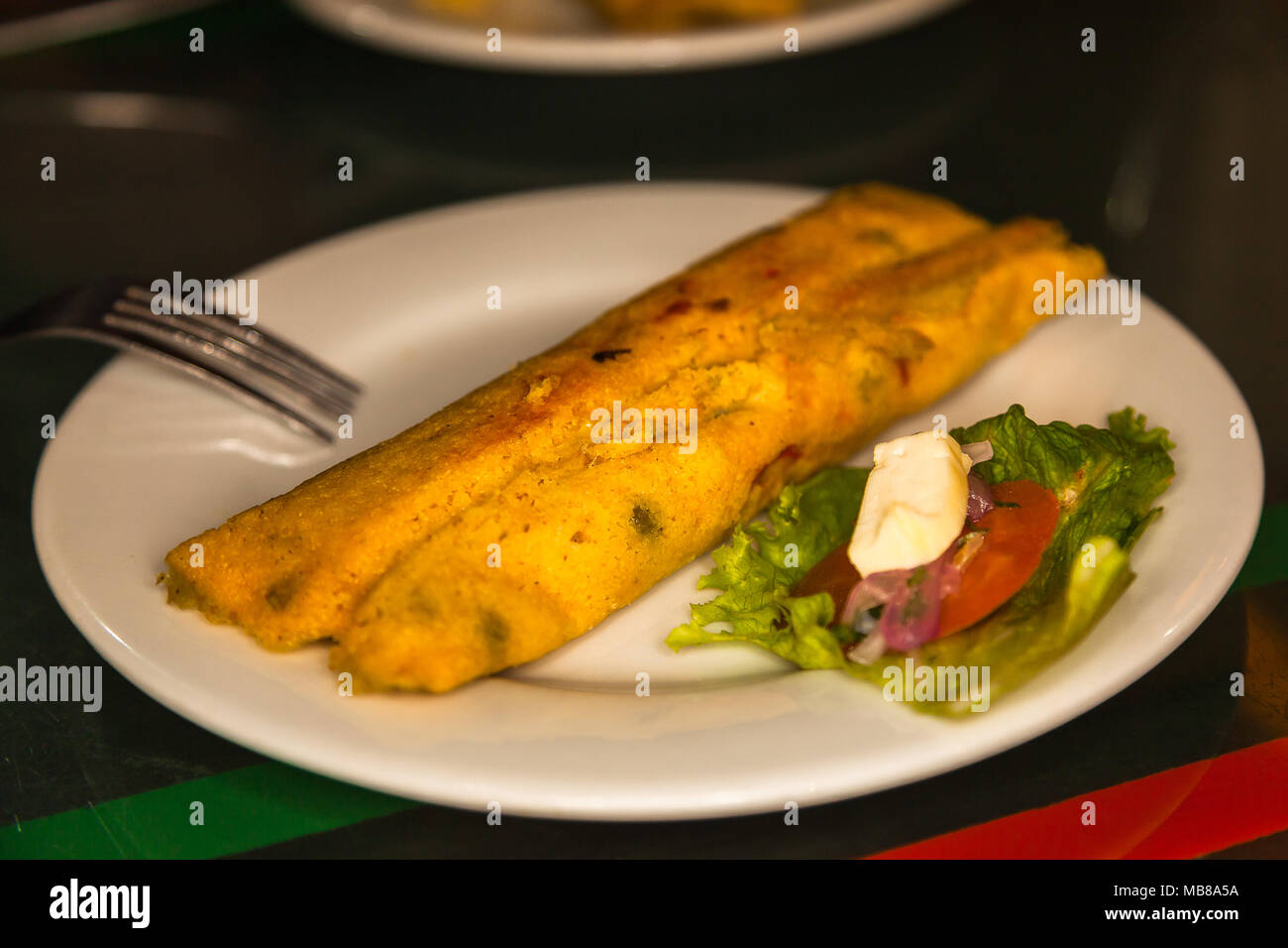Tamales lojanos. Yellow corn cake served on a white plate with lettuce and tomato Stock Photo