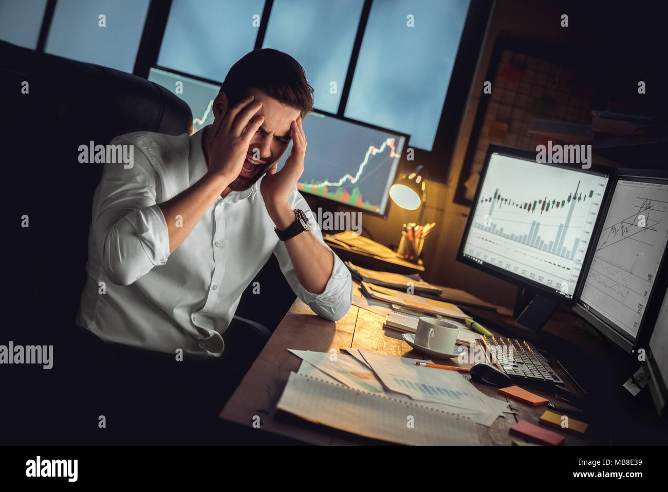 Young bearded man trader at office sitting at table having headache painful touching head Stock Photo