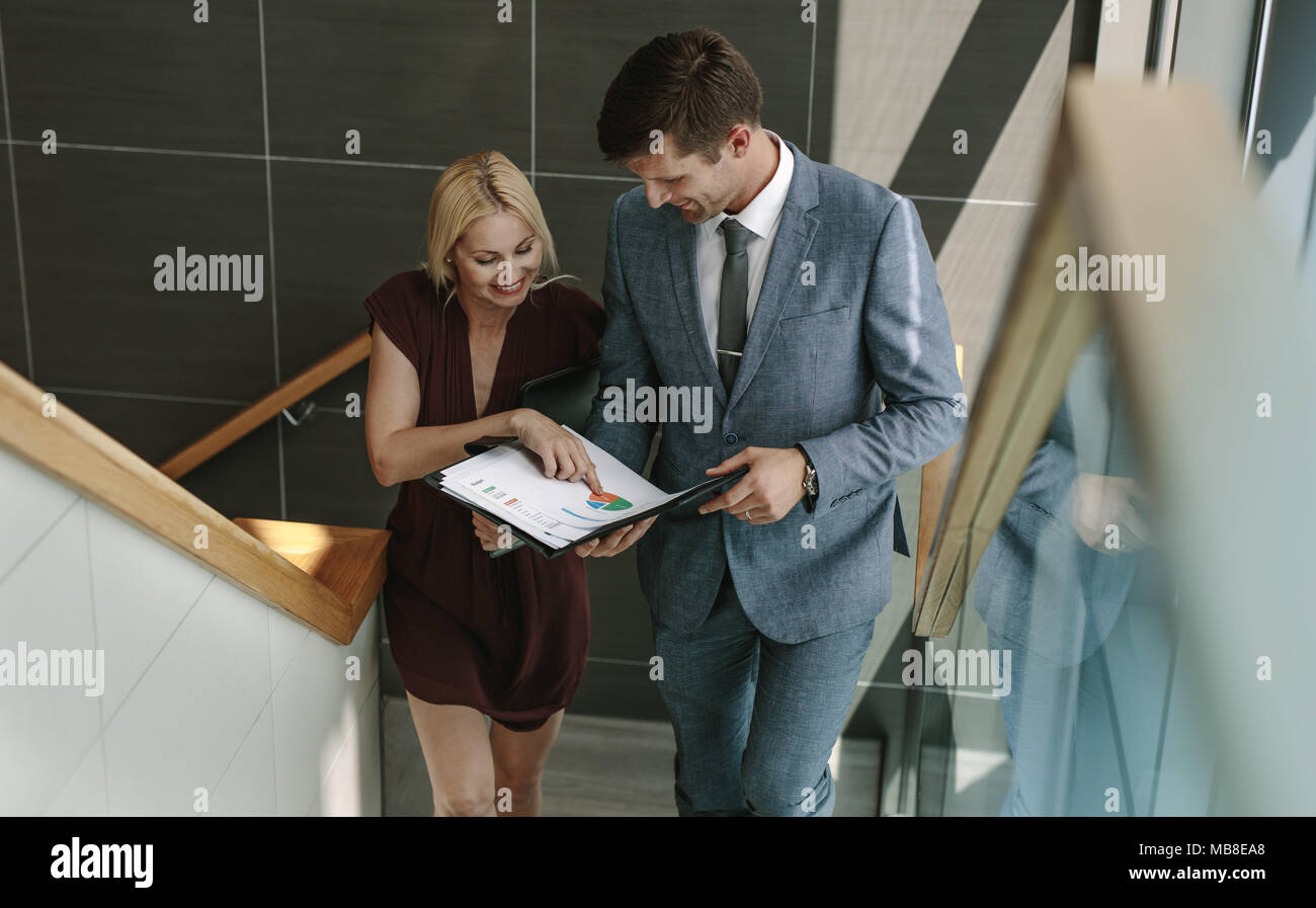 Young businesswoman discussing over a document with her colleague on stairs in the office building. Two business people walking up the steps and talki Stock Photo